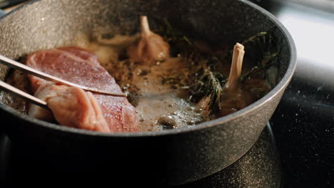 piece of meat layed in cast iron pot with sizzling oil garlic and rosemary