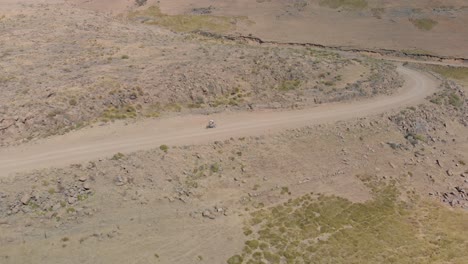 aerial shot following a mountain biker climbing up a pass on a gravel road