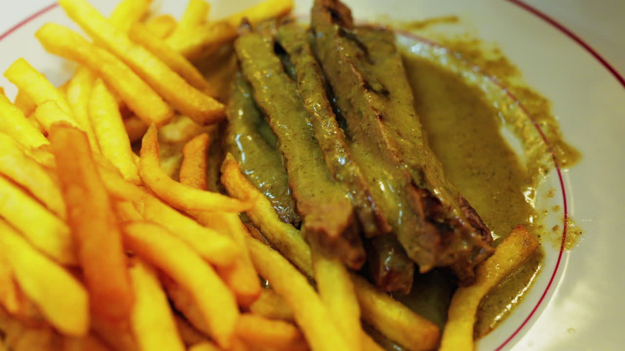Close up of a plate of fries with meat and green sauce on a plate