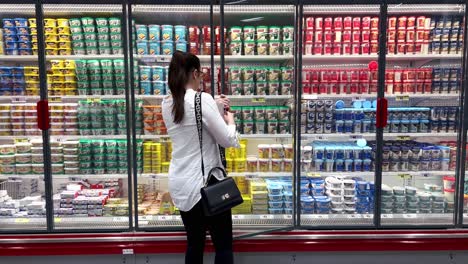 woman selects dairy products from a refrigerator in a supermarket