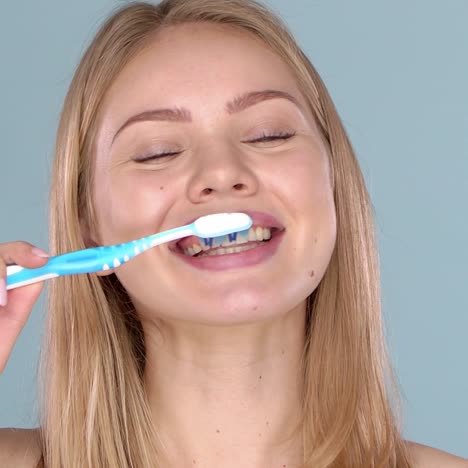 Woman-with-adorable-smile-brushing-her-teeth--isolated-on-blue-background