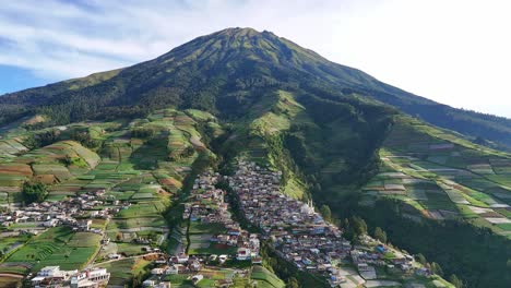 drone footage of a majestic green mountain with farmlands and clustered village houses under bright daylight. nepal van java, mount sumbing, indonesia