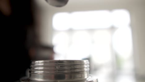 silueta de una persona que vierte café en polvo en una cafetera de metal plateado