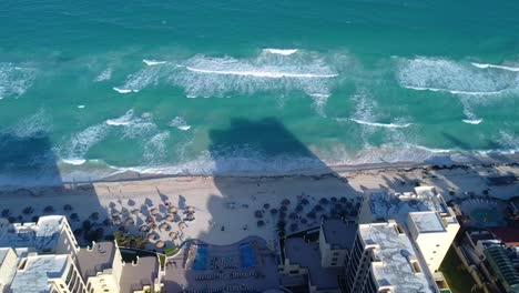 Aerial-high-view-of-blue-Caribbean-Sea-and-its-waves-breaking-on-white-sand-beach-in-Cancun-hotel-zone,-Mexico