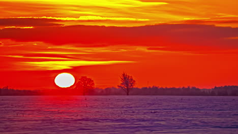 bright colorful, orange and crimson sunrise over snow on a winter farmland field - time lapse