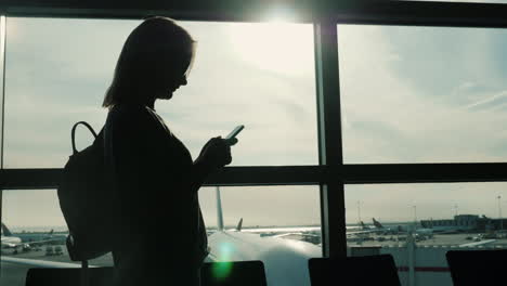 silhouetted woman using smartphone in airport