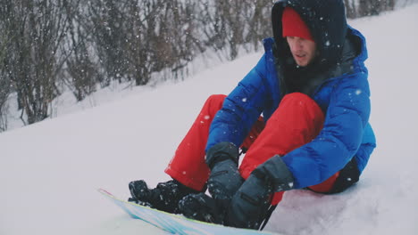 a man in red pants sitting on the snow fastens snowboard boots on the ski slope