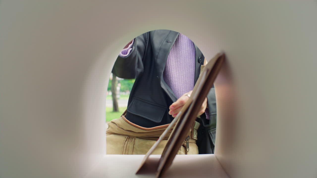 Postal Worker Placing Envelopes and Parcel into Mailbox during Delivery Round