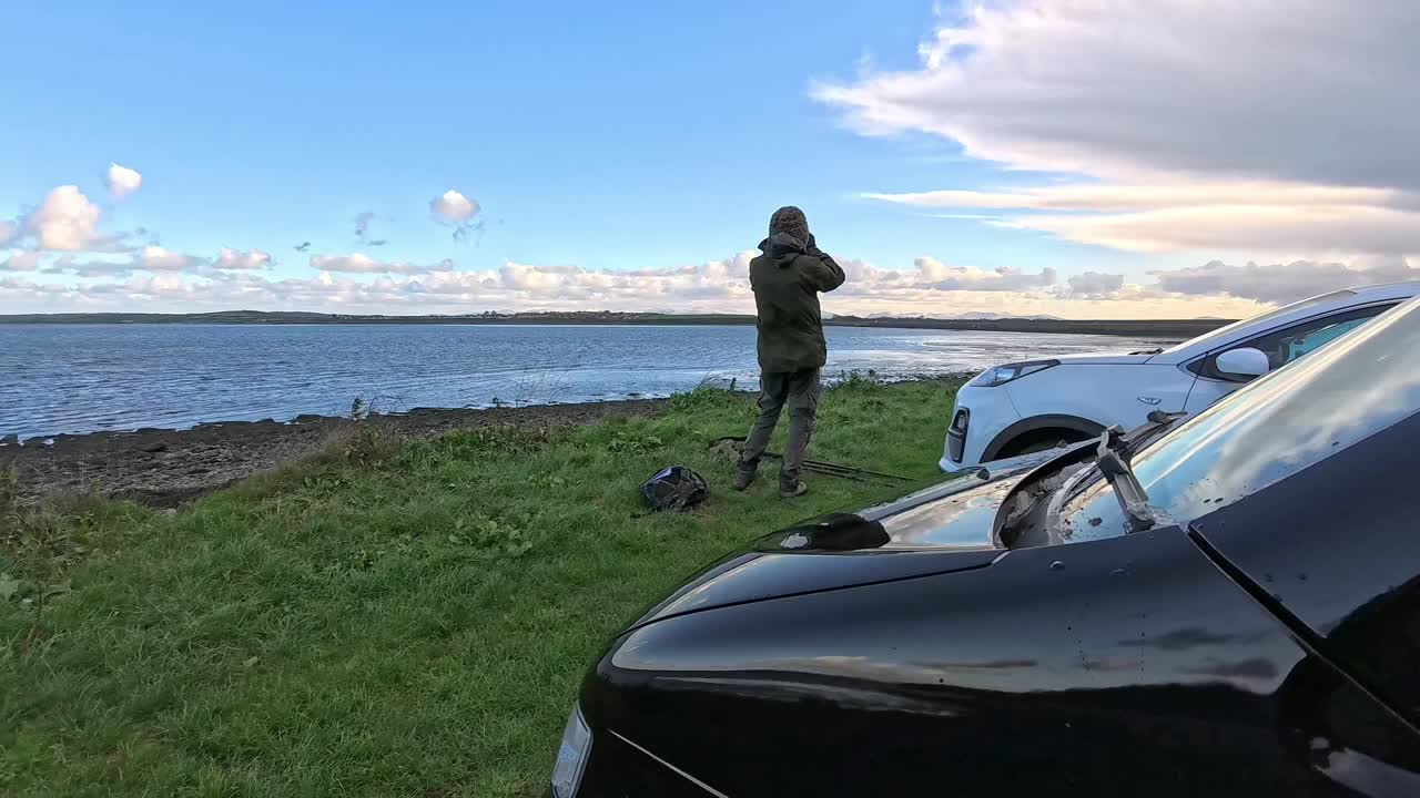 Man watching incoming storm clouds with binoculars in front of campervan on the welsh coast