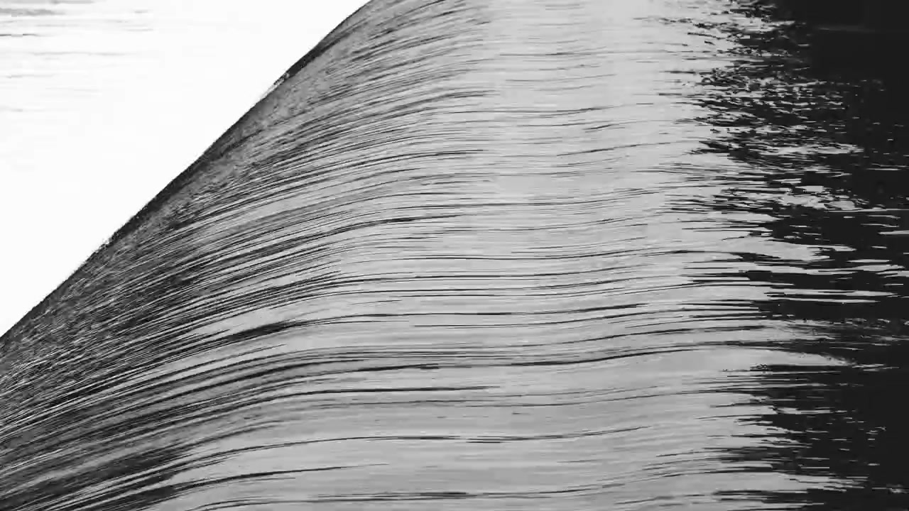Close up of water flowing over spillway at Loch Faskally Dam in Pitlochry, highlighting smooth water texture, continuous flow, and monochrome pattern