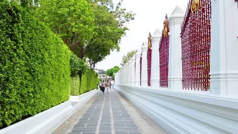 a serene walk along wat pho's colorful pathway in bangkok, thailand. bright greenery and ornate architecture under soft daylight