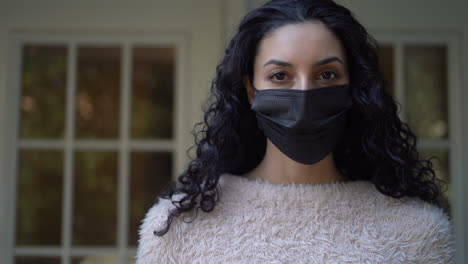 beautiful young latina woman wearing a black face mask and looking directly at the camera