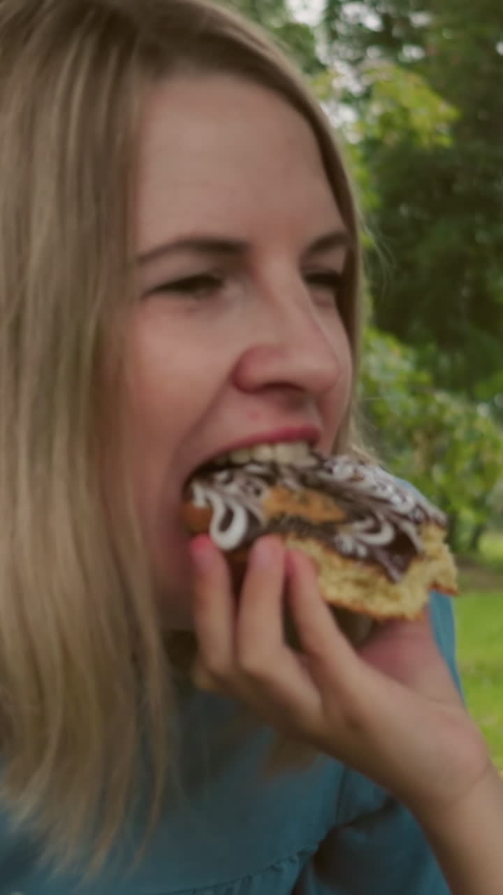 un primer plano de una mujer tomando un bocado de un pastel cubierto de chocolate, con una mano que se lo ofrece a ella
