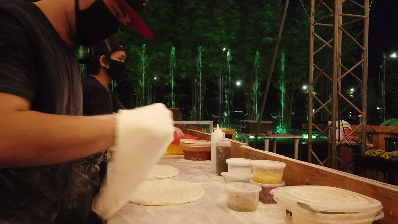 3 men preparing Pizza dough on a metal table with water fountain lighted in the background.
