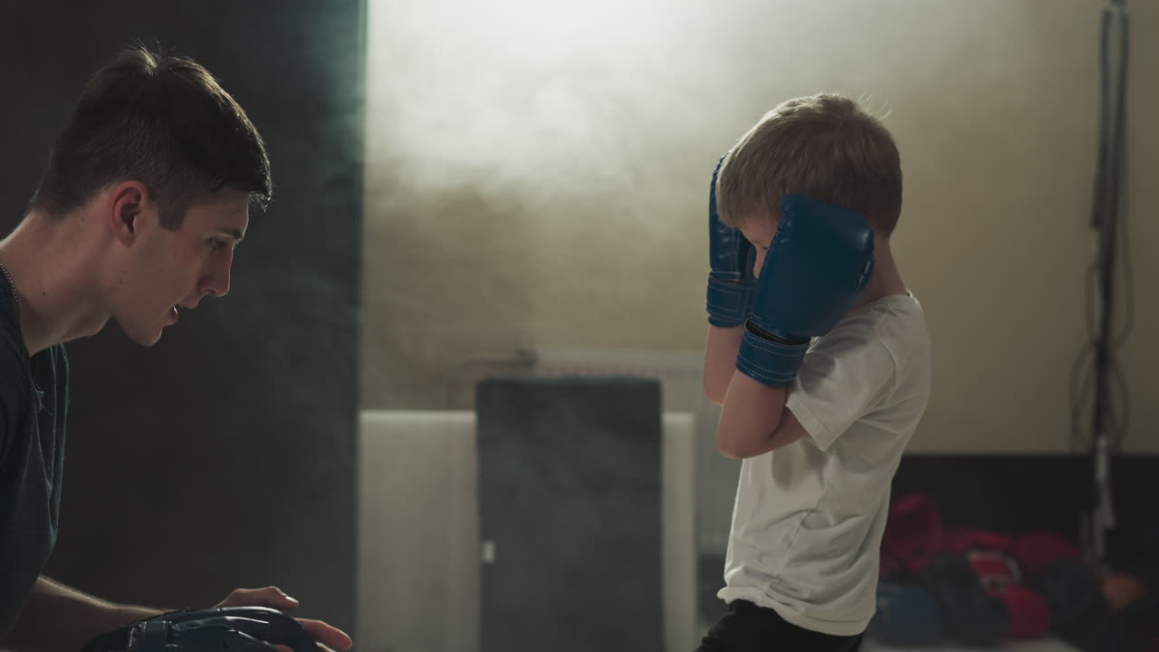Child does kicks with instructor in martial arts gym. Young trainer conducts kickboxing lesson with toddler boy in sports center slow motion. Healthy life