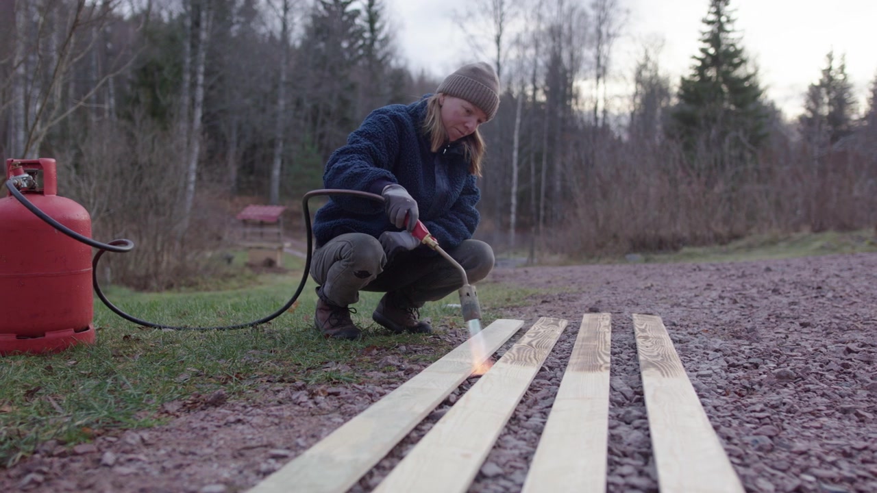 Händig kvinna använder blåslampa med gasol för att förkola och bevara träplankor