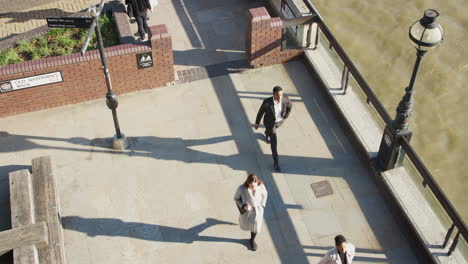 vista elevada de tres trabajadores de la ciudad caminando por una calle urbana soleada junto al río támesis en la ciudad de londres, bloqueo