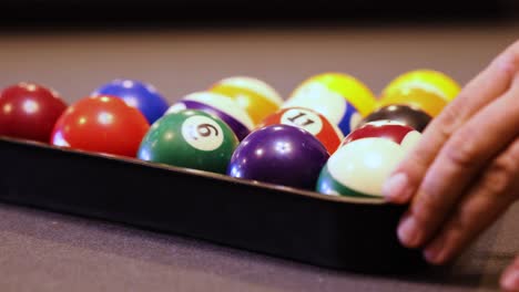 hands placing pool balls inside triangle on the billiard table