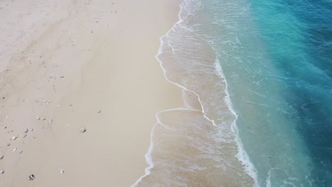aerial drone reversing over white sandy beach, turquoise ocean water, and waves on jaco island, timor-leste, southeast asia