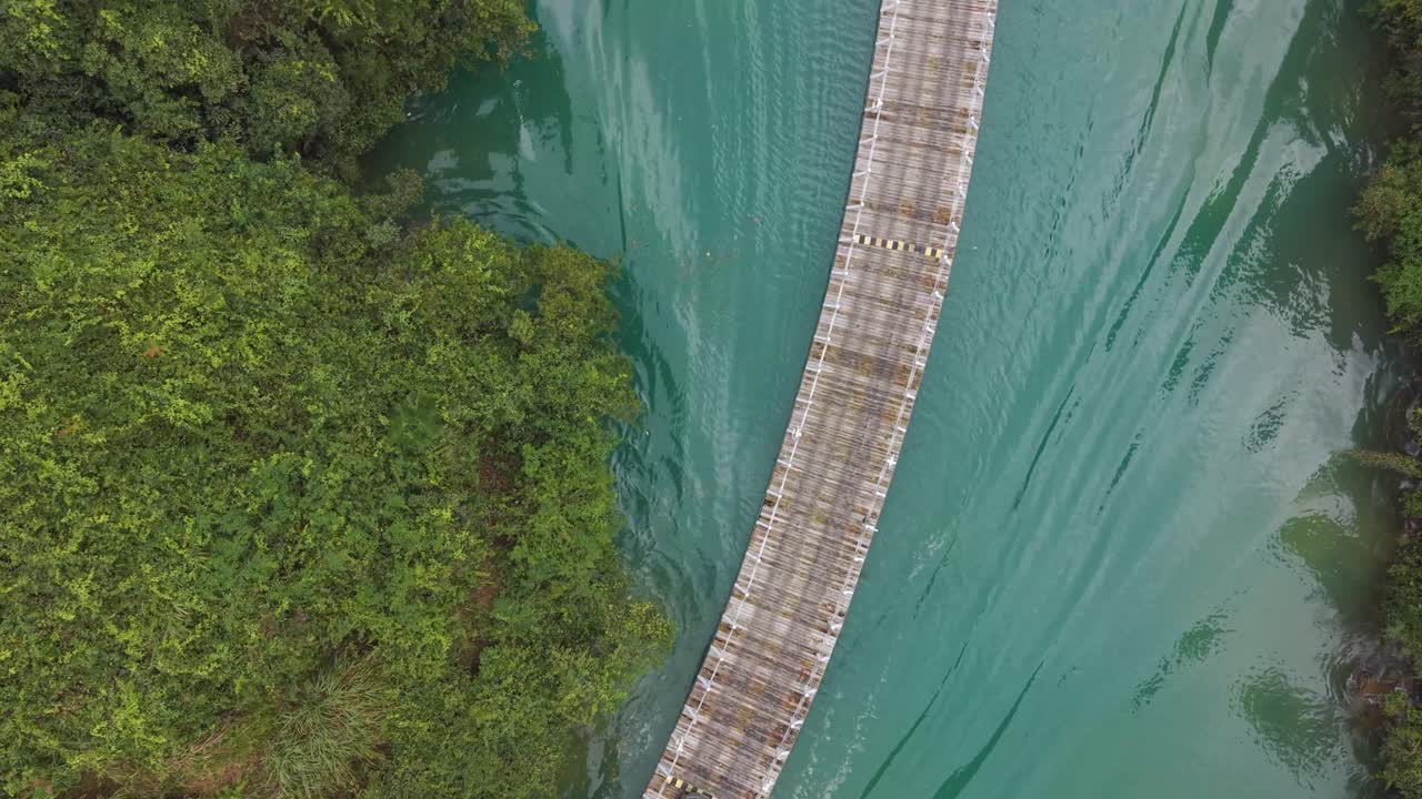 Top-down drone shot of the Shiziguan floating bridge in Hubei, China, showing cars crossing over green river water surrounded by dense forest and mountains