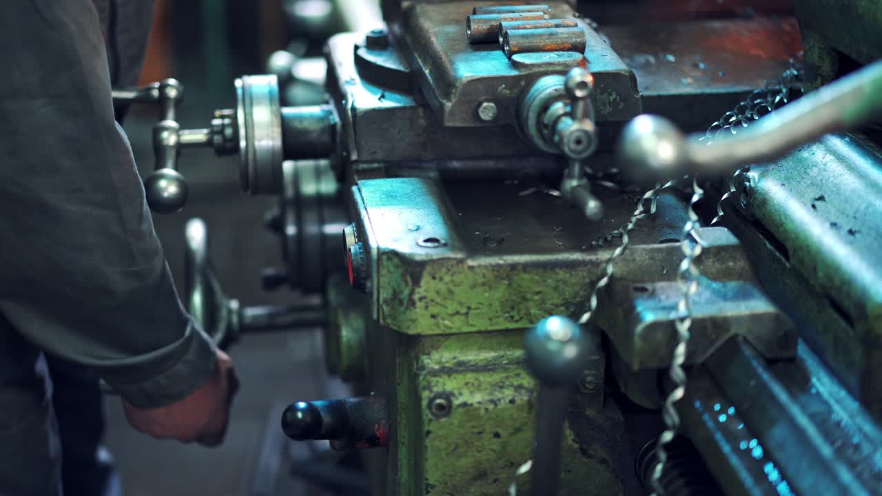 Machine operator turns on an industrial machine. Man employee working with turning lathe and metalworking machine at manufacturing hall at industrial factory