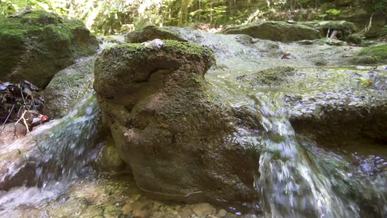 toma panorámica derecha de correr agua dulce desde las montañas hacia las rocas cubiertas de musgo en verano