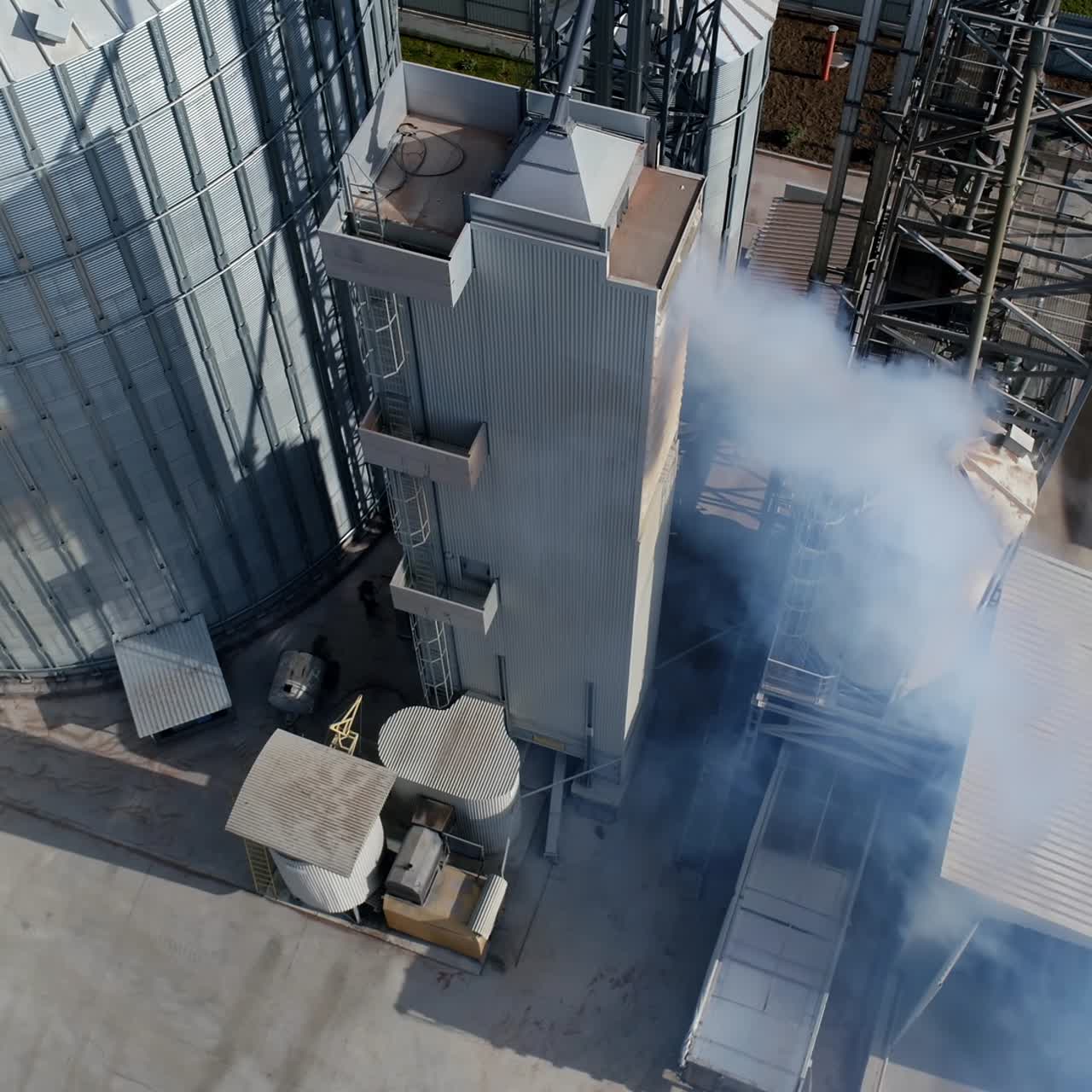 Modern warehouse from the air. Industrial factory with grain elevators. White vapor from manufacturing pollute the atmosphere. Aerial view