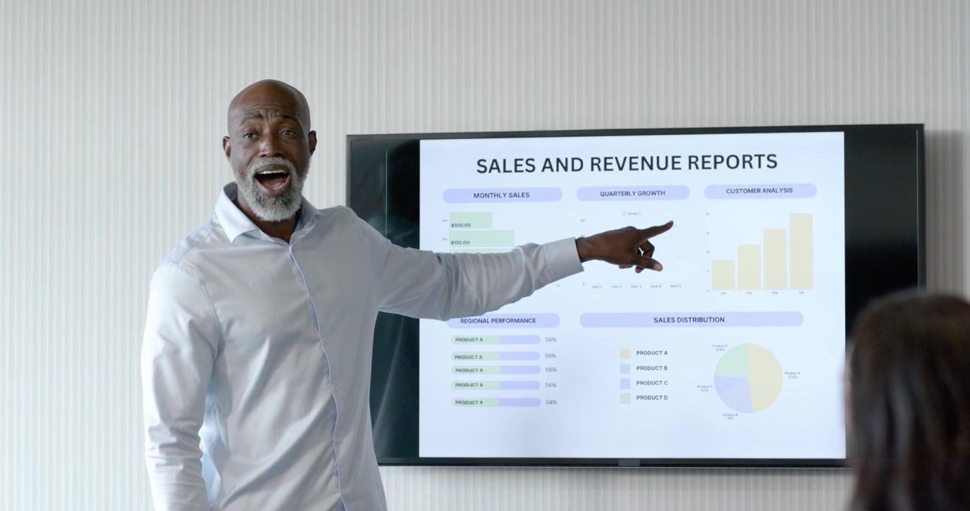 African American man entering meeting room, pointing at sales charts on screen, explaining trends