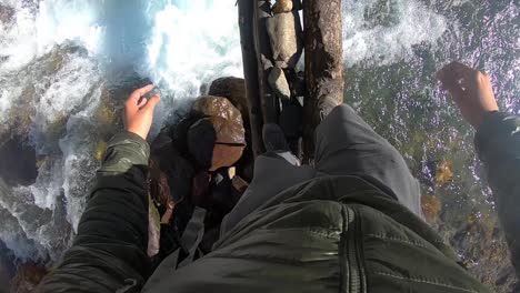 an amateur, solo backpacker attempting to cross a dangerous, fast flowing mountain river stream by slowly stepping on a wooden log