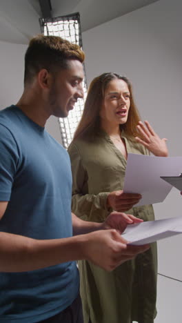 vertical video of female film director talking with male and female actors holding scripts rehearsing for shooting movie or video in studio