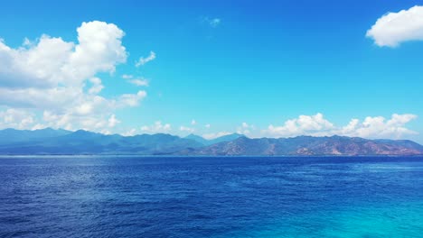 Beautiful-white-fluffy-clouds-over-the-mountains-and-deep-blue-tropical-sea,-Bali,-Indonesia