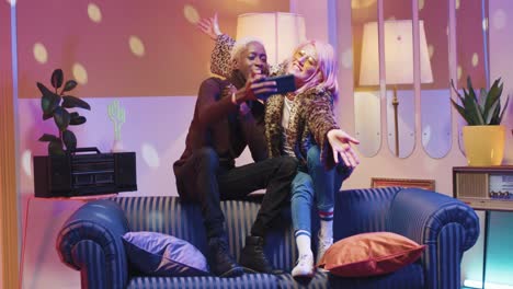 african american man and caucasian stylish woman in sunglasses making a selfie sitting on couch in a retro party at home