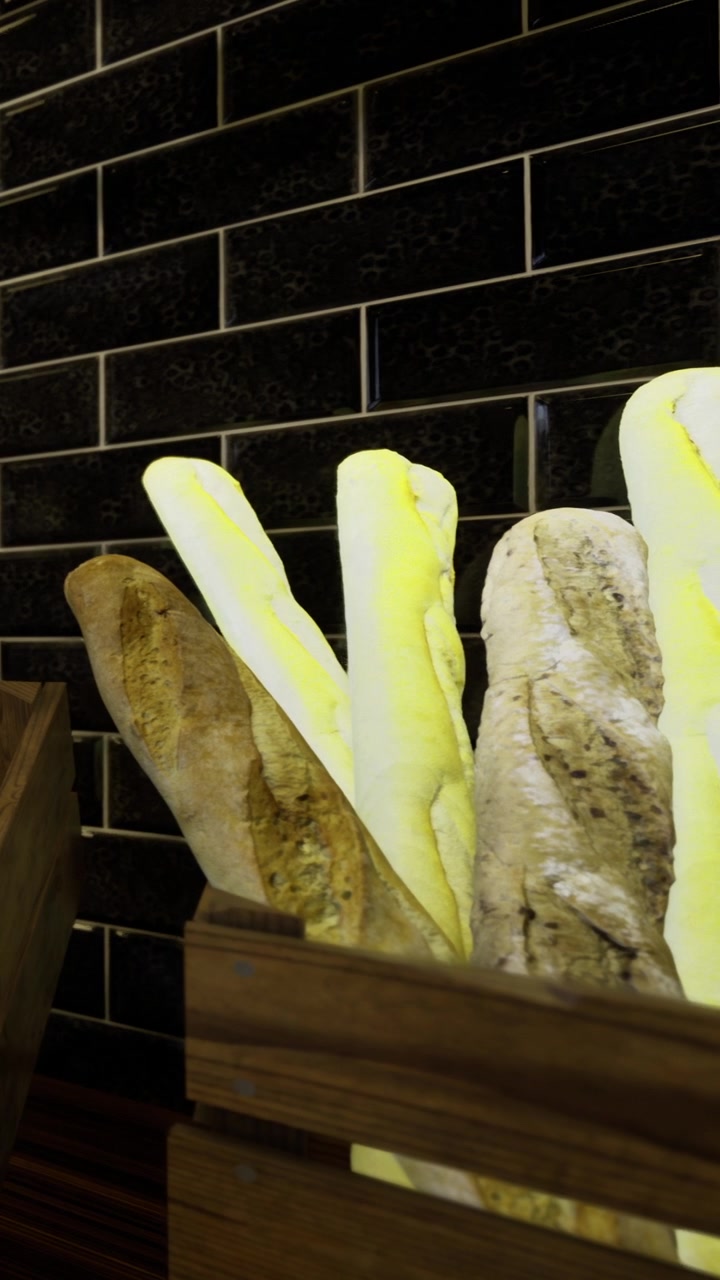 Vari tipi di pane in un cesto di legno contro una parete di piastrelle scure.