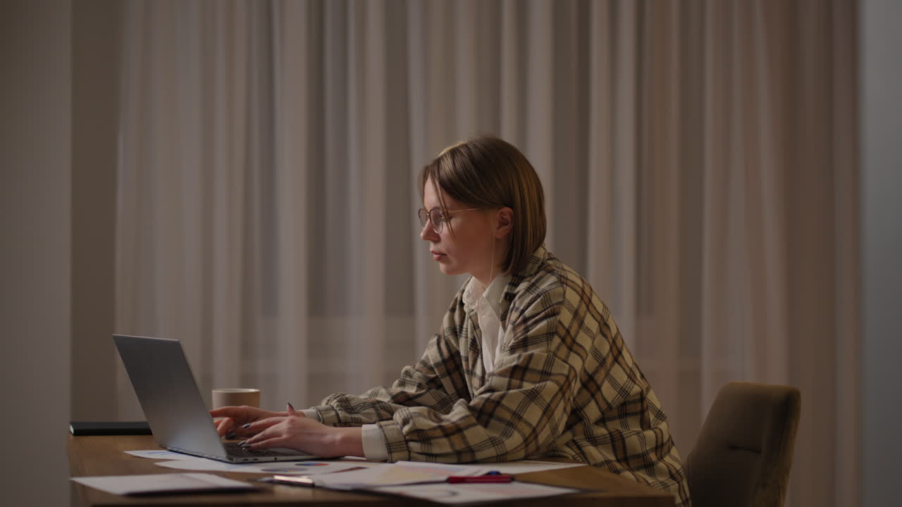 A girl works from home or a student is studying from home or a freelancer. She uses a laptop and a phone. girl sit at desk in living room study on laptop making notes concentrated young woman work