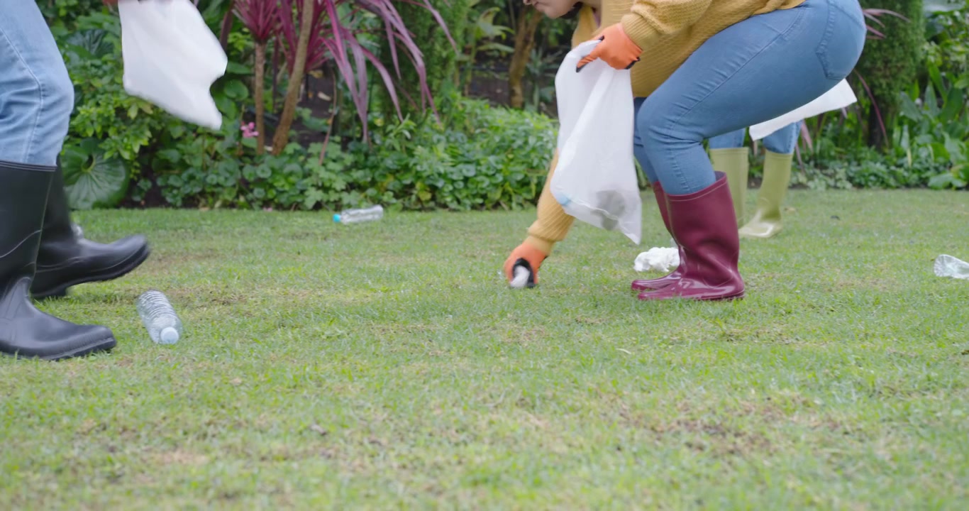 Male and female volunteers seeing litter walking on lawn, picking bottles with gloves for cleanup