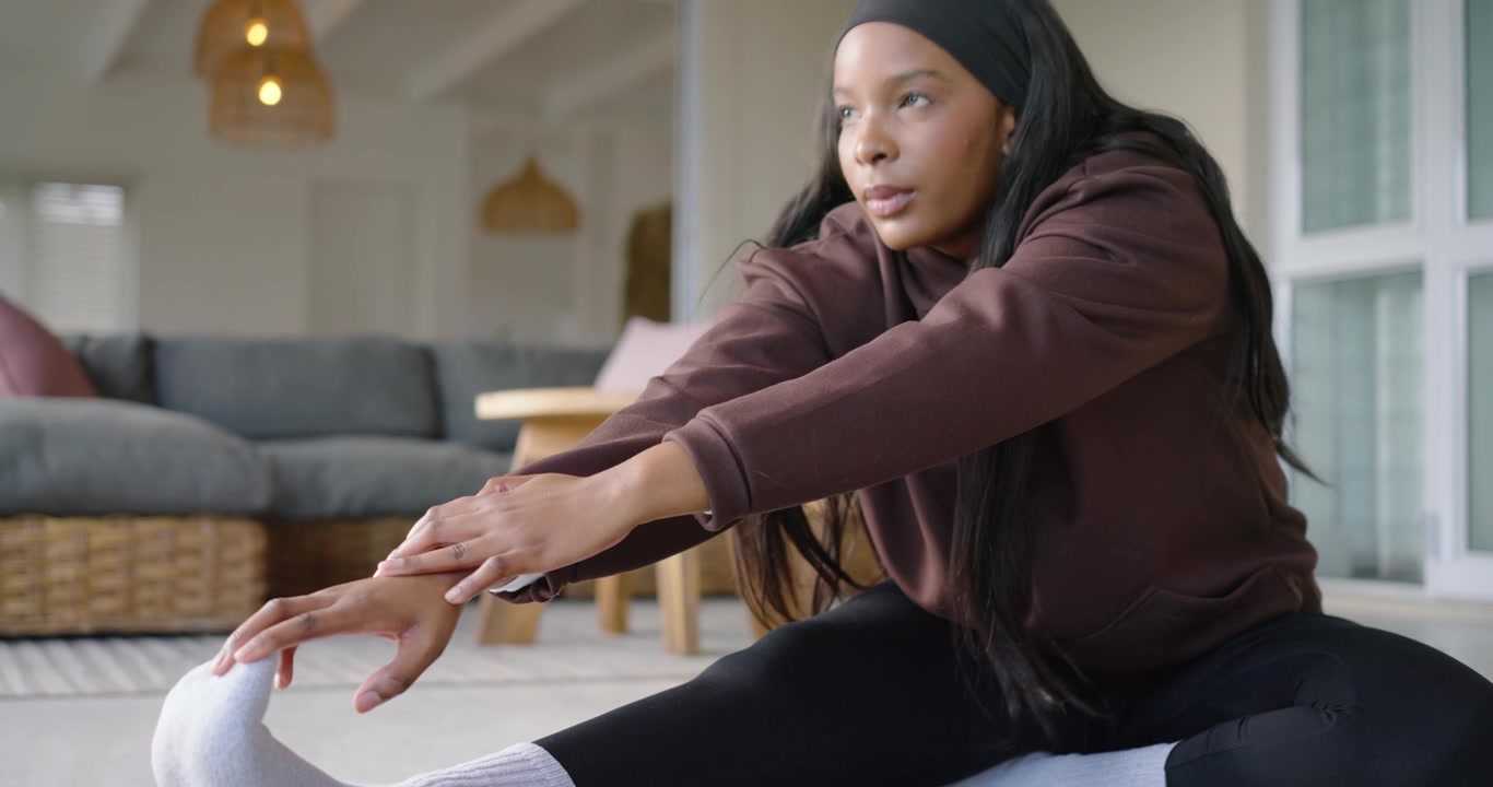 Efter opvarmning laver afroamerikansk kvinde siddende strækøvelser på sort måtte derhjemme, iført hættetrøje og hvide sokker