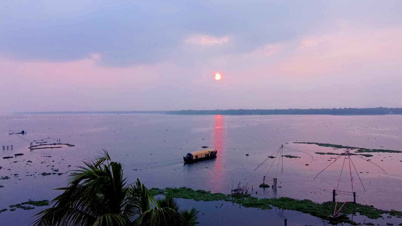 Tramonto sulle tranquille backwaters del Kerala, in India, con una tradizionale casa galleggiante e reti da pesca cinesi