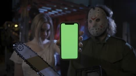 jason voorhees and woman holding green screen smartphone in horror setting