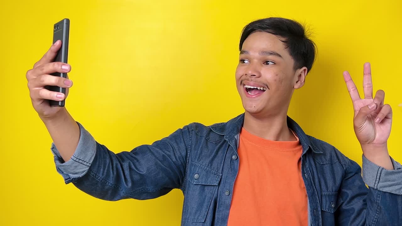 젊은 vlogger 남자가 인사 구독자를 말하고 평화 손가락을 보여, 노란색 배경에 고립