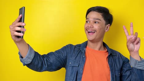 Young-vlogger-man-saying-hi-greeting-subscriber-and-showing-peace-finger,-isolated-on-yellow-background