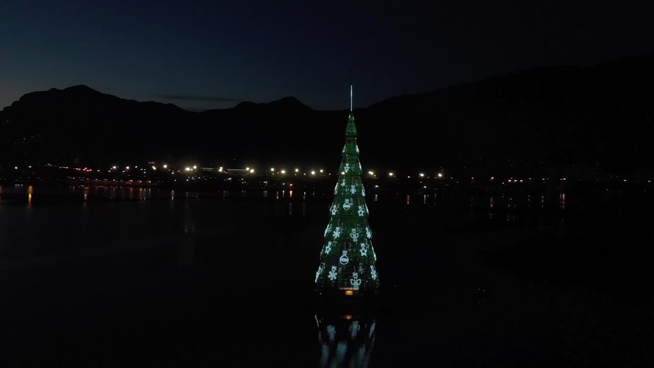 리오 데 자네이로의 불빛이 있는 떠다니는 크리스마스 트리는 도시의 실루엣 뒤에 있고 도시 호수에 있는 나무의 반사와 함께 일몰에 있습니다.