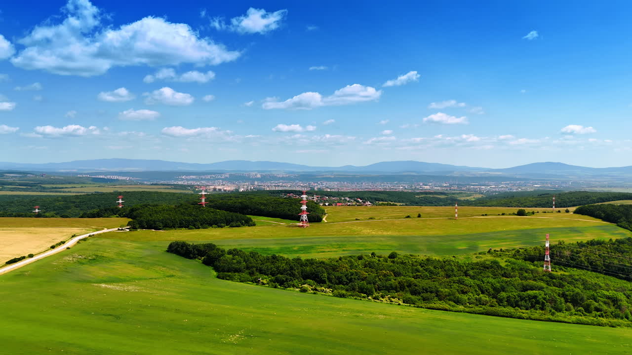 Green hills with signal towers. Green fields stretch under a blue sky, with communication towers on the horizon in a serene rural landscape