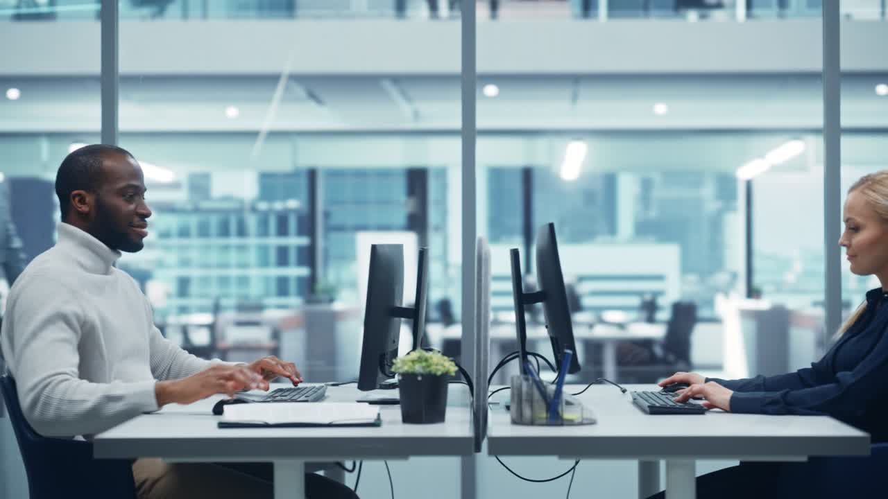 oficina multiétnica moderna: ingeniera informática profesional negra que trabaja en una computadora de escritorio frente a una especialista en ciencias de la computación caucásica. lugar de trabajo diverso con sensación corporativa pero espíritu creativo