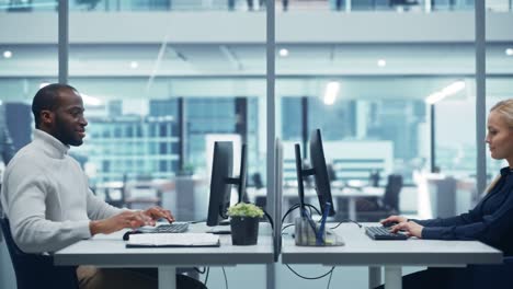 moderno ufficio multietnico: ingegnere informatico professionista nero che lavora su un computer desktop di fronte a una specialista di informatica caucasica femminile. luogo di lavoro diversificato con sensazione aziendale ma spirito creativo