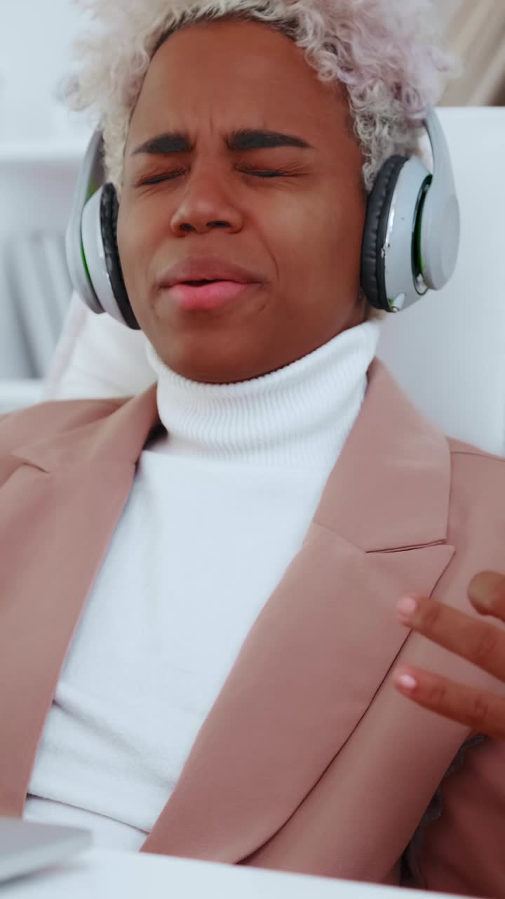 Young female wearing headphones closes eyes and listens to music at desk
