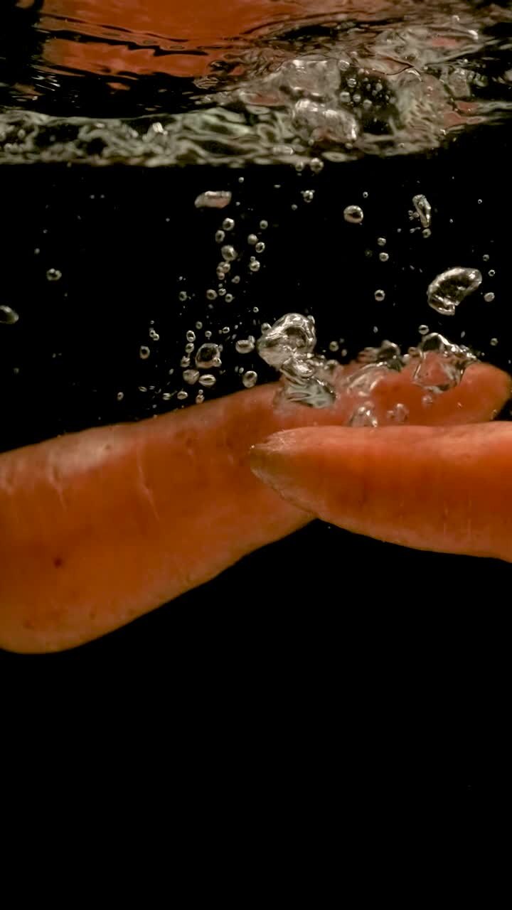 Fresh Carrots Falling into Water with Bubbles