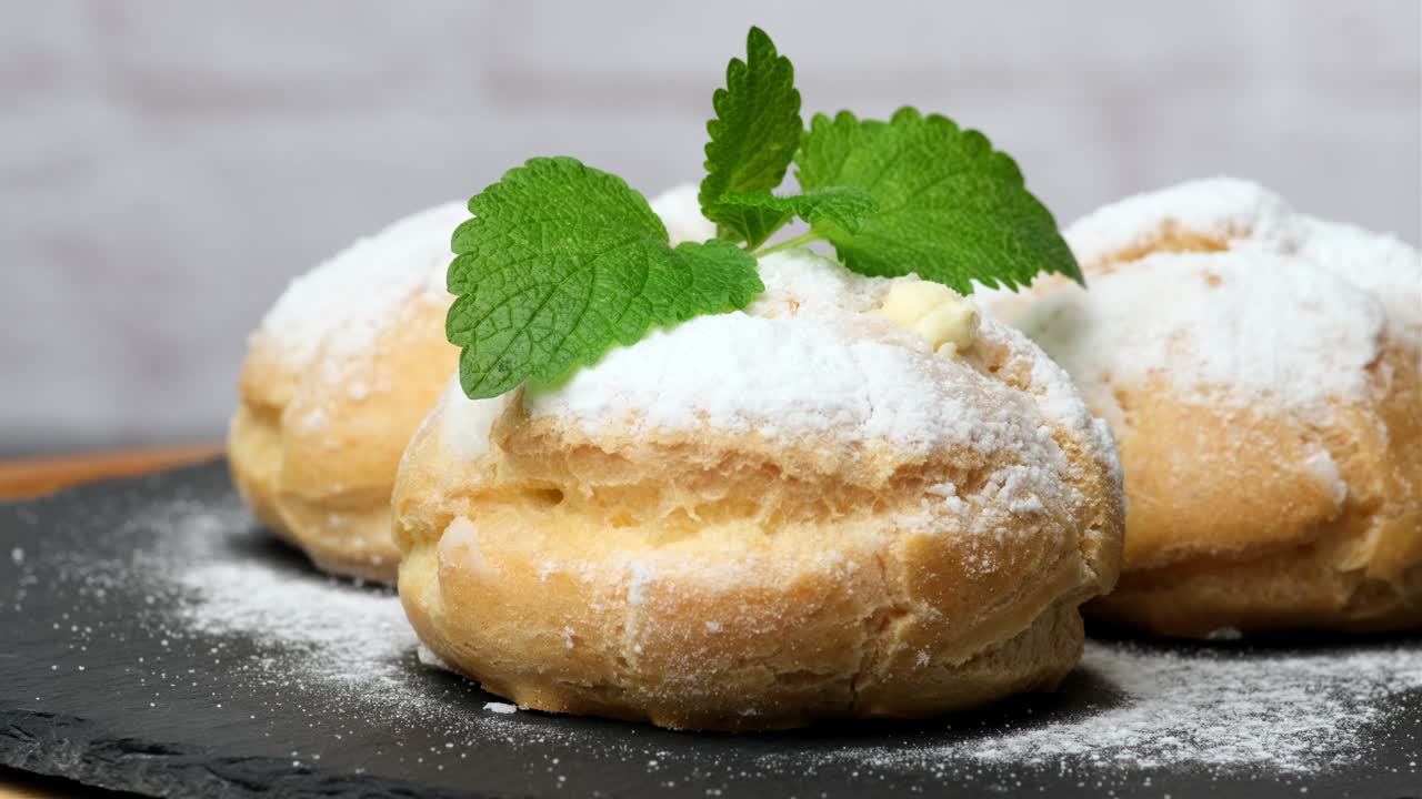 baked custard eclairs and sprinkled with powdered sugar and decorated with a mint leaf on a black board