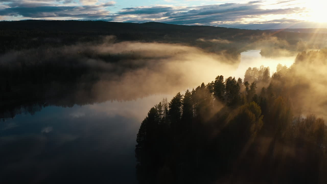 An aerial shot of a majestic sunset over a river running through a pine tree forest