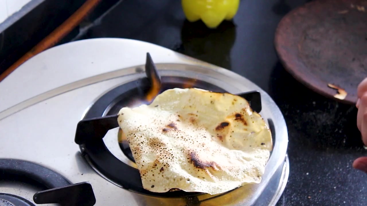Primo piano verticale di papad che arrostisce direttamente sulla fiamma del gas in una cucina indiana. Perfetto per tutorial di cucina, cucina indiana, video di ricette, blog di cucina e preparazione di pasti tradizionali