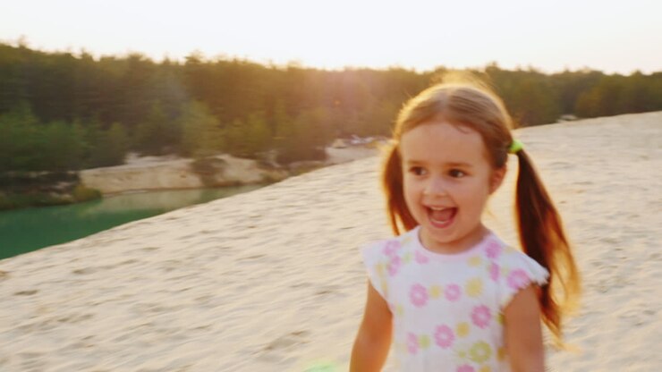 Bambina allegra e spensierata di tre anni che corre sulla sabbia sullo sfondo di bellissimi laghi.
